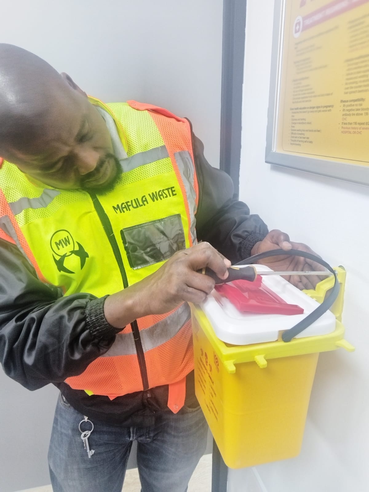 Mafula Waste technician safely servicing a wall-mounted sharps container at a clinic